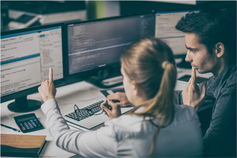 Two people sitting at a desk with computers.